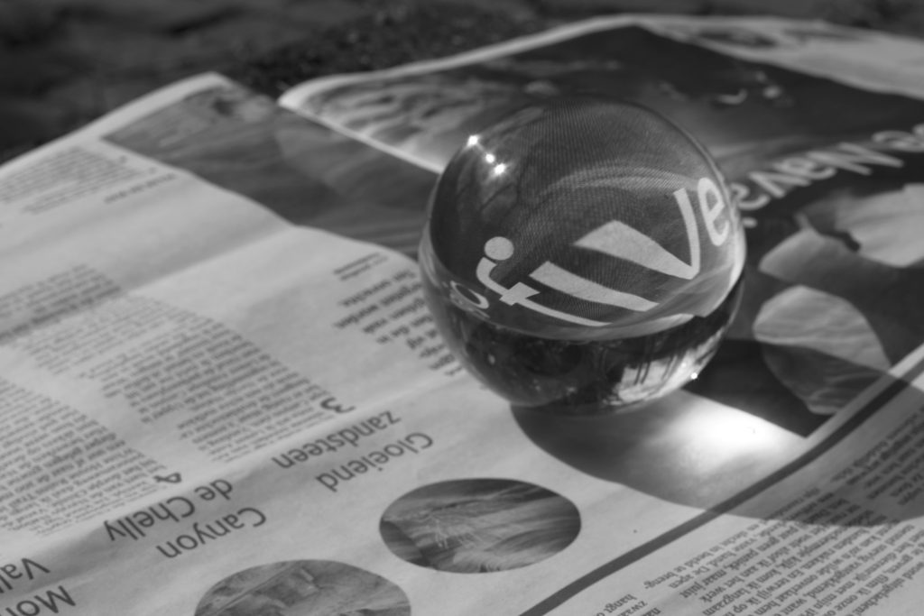A glass sphere magnifies text on a newspaper in a close-up black and white photo.